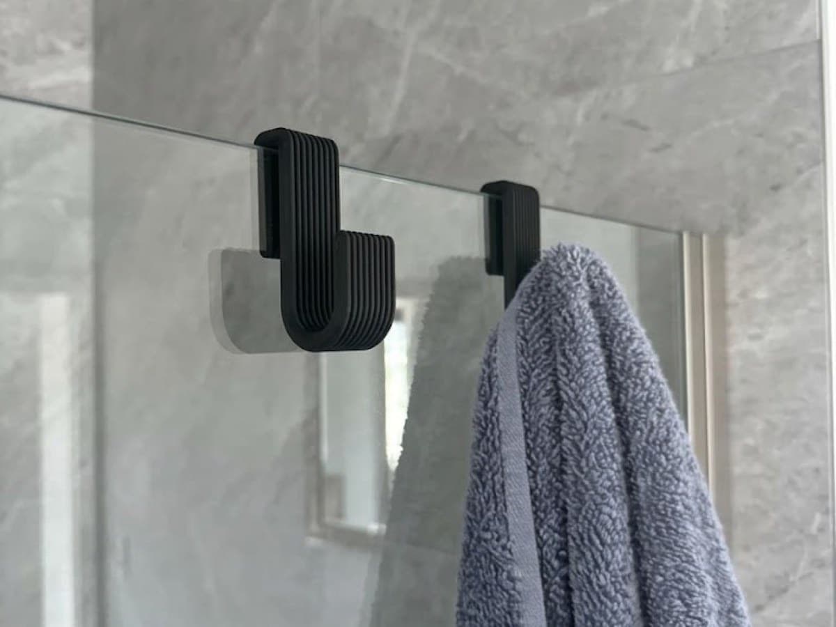 Deux crochets noir mat glissés sur la paroi vitrée d'une douche, l'un portant une serviette