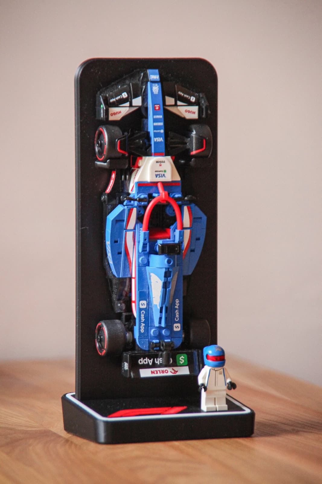 Support vertical noir carbone avec une monoplace de Formule 1 LEGO Speed Champions dressée à la verticale et sa minifigurine posée sur le socle